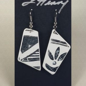 May include: A pair of white ceramic earrings with black geometric designs. The earrings are dangle style with silver hooks.