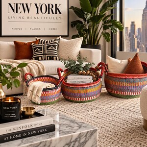 May include: Three round, hand-woven baskets featuring a vibrant, multi-coloured striped pattern with red handles. The baskets are arranged in a row, with the largest on the right, containing decorative cushions and books, while the smaller ones hold textiles.