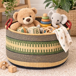 Peut inclure: Un panier de rangement rond en osier avec un motif géométrique vert et noir, rempli de jouets. Comprend un ours en peluche, une peluche éléphant, des anneaux en bois empilables, une couverture à motifs d'étoiles et des blocs en bois. Le panier a des poignées rouges.