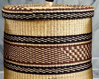 May include: A woven storage basket with a black handle and brown and black stripes. The basket has a round base and stands on four wooden feet.
