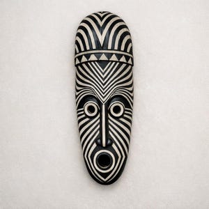May include: A black and white tribal mask with a long, oval shape. The mask features a series of striped patterns and circular eyes. The mouth is wide open. The top of the mask has a rounded shape.