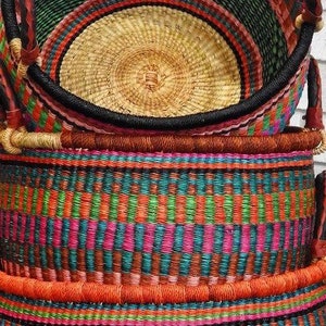 May include: A stack of three round woven baskets featuring a vibrant multicoloured pattern of pink, teal, green, and orange vertical stripes. Each basket has a thick, dark-coloured rim and sturdy handles wrapped in a contrasting light-coloured material.