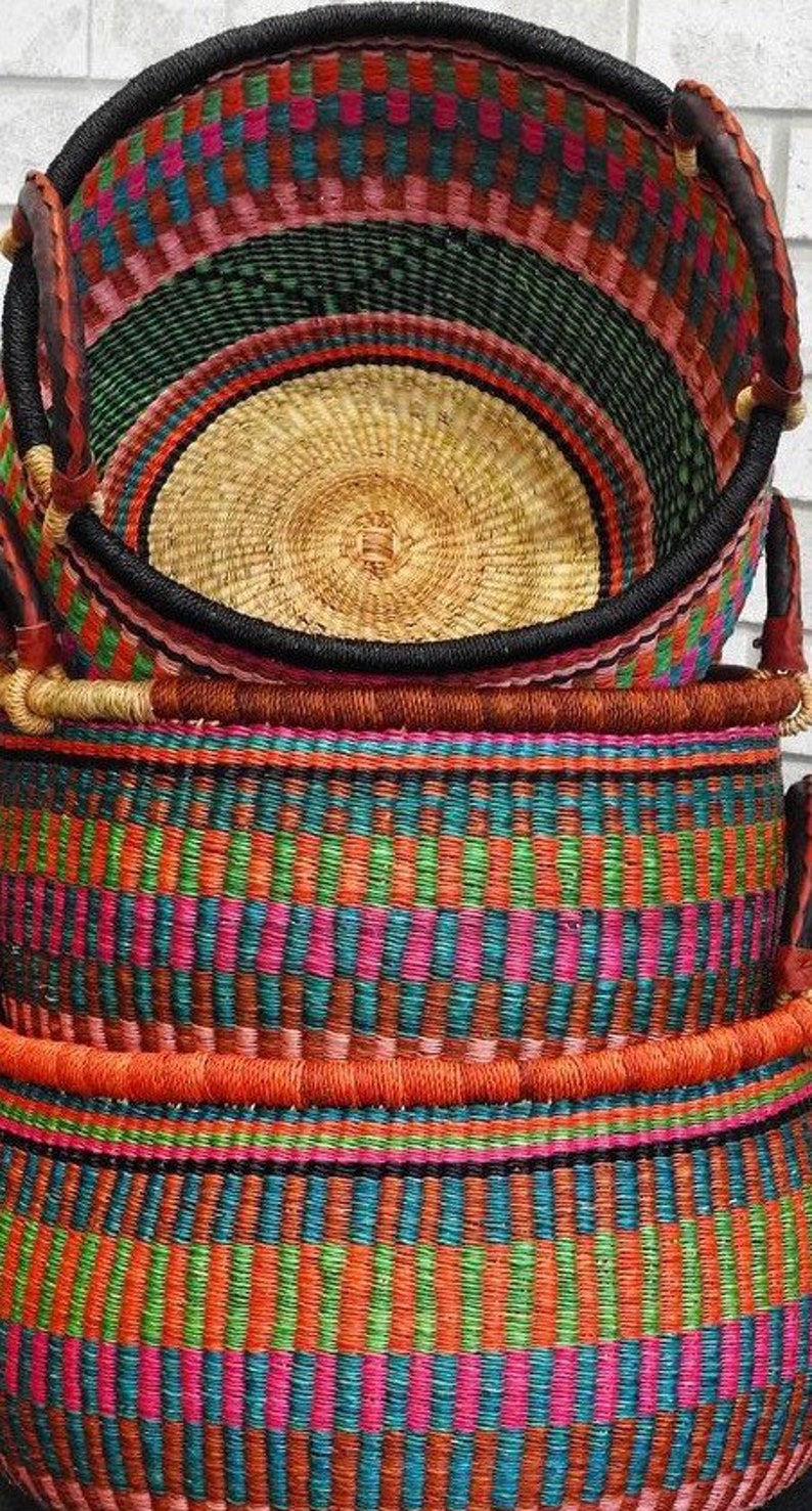 May include: A stack of three round woven baskets featuring a vibrant multicoloured pattern of pink, teal, green, and orange vertical stripes. Each basket has a thick, dark-coloured rim and sturdy handles wrapped in a contrasting light-coloured material.