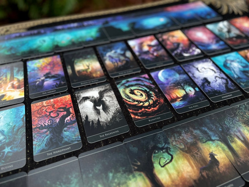 Op de afbeelding: Een set tarotkaarten met kleurrijke, abstracte kunstwerken. Elke kaart heeft een uniek ontwerp met een titel onderaan. De kaarten liggen op een zwart oppervlak.