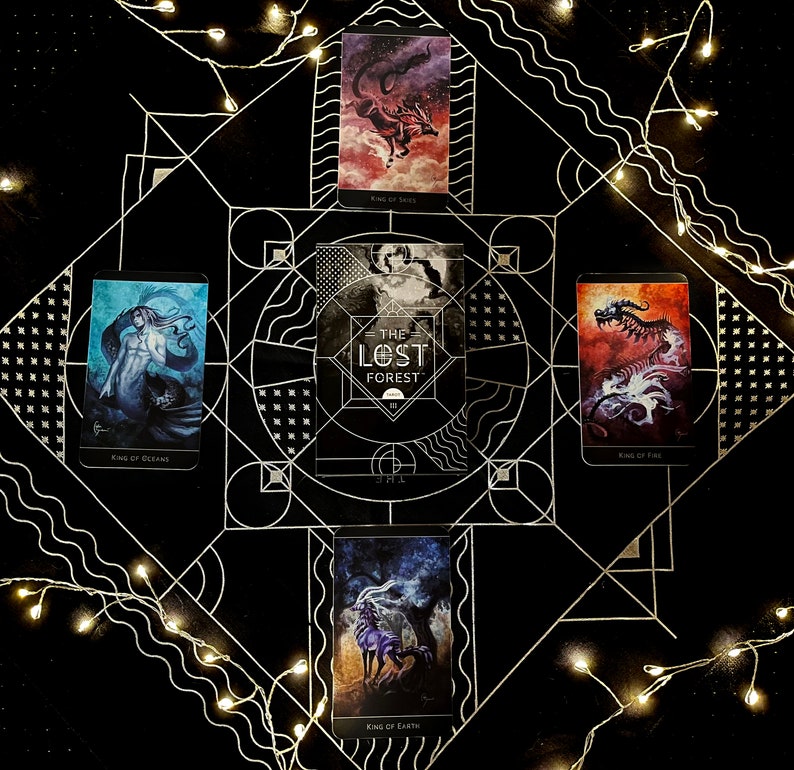 Op de afbeelding: Tarotkaartlegging op een zwarte achtergrond met witte lichtslingers. De kaarten zijn uit het The Lost Forest Tarot deck en bevatten de Koning van de Oceanen, de Koning van Vuur, de Koning van Aarde en de Koning van Zeilen. De middelste kaart is de The Lost Forest kaart.