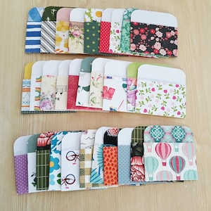 May include: A collection of colorful, patterned paper envelopes. The envelopes feature a variety of designs, including floral, geometric, and striped patterns. The envelopes are arranged in neat rows on a light wooden surface.