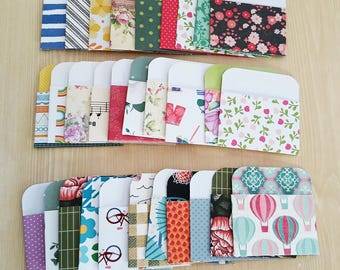 May include: A collection of colorful, patterned paper envelopes. The envelopes feature a variety of designs, including floral, geometric, and striped patterns. The envelopes are arranged in neat rows on a light wooden surface.