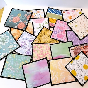 May include: A collection of square paper cards with floral and patterned designs. Each card has a black border and features various colors, including pink, blue, yellow, and green. The cards are arranged on a white surface, showcasing a variety of botanical and abstract patterns.