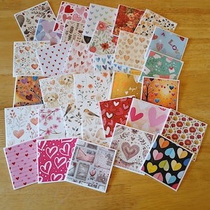 May include: A collection of square cards with various designs, including hearts, floral patterns, birds, and the word "Love". The cards feature a mix of colors, such as red, pink, blue, and yellow, and are arranged on a wooden surface.