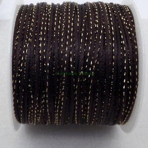 May include: A spool of dark brown satin cord with gold metallic accents. The cord is tightly wound on a white plastic spool. The gold accents are evenly spaced along the length of the cord, creating a shimmering effect. Ideal for jewelry making and crafts.