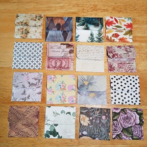 May include: A collection of sixteen small, square paper envelopes with various decorative patterns. Designs include floral, geometric, landscape, and abstract prints in a range of colors, arranged on a wooden surface.