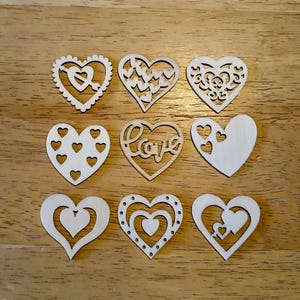 May include: Nine wooden heart cutouts in various designs, including hearts with arrows, heart-shaped cutouts, and the word "Love". The hearts are arranged on a light brown wooden surface, perfect for crafts and decorations.