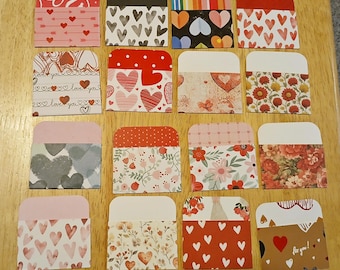 May include: A collection of small, decorative paper envelopes with various patterns. Designs include hearts, floral prints, and the text "love you." The envelopes are in shades of red, pink, and brown, perfect for crafting or gifting.