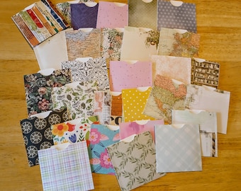 May include: A collection of small, decorative paper envelopes in various patterns and colors. Designs include floral, map, polka dot, and plaid. The envelopes are arranged on a wooden surface, showcasing a variety of textures and styles.