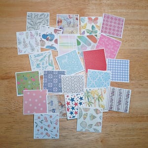 May include: A collection of square paper tiles featuring a variety of printed patterns including floral motifs, blue pumpkins, butterflies, pink polka dots, red stars, blue gingham, palm trees, seashells, cherries, and various geometric designs.