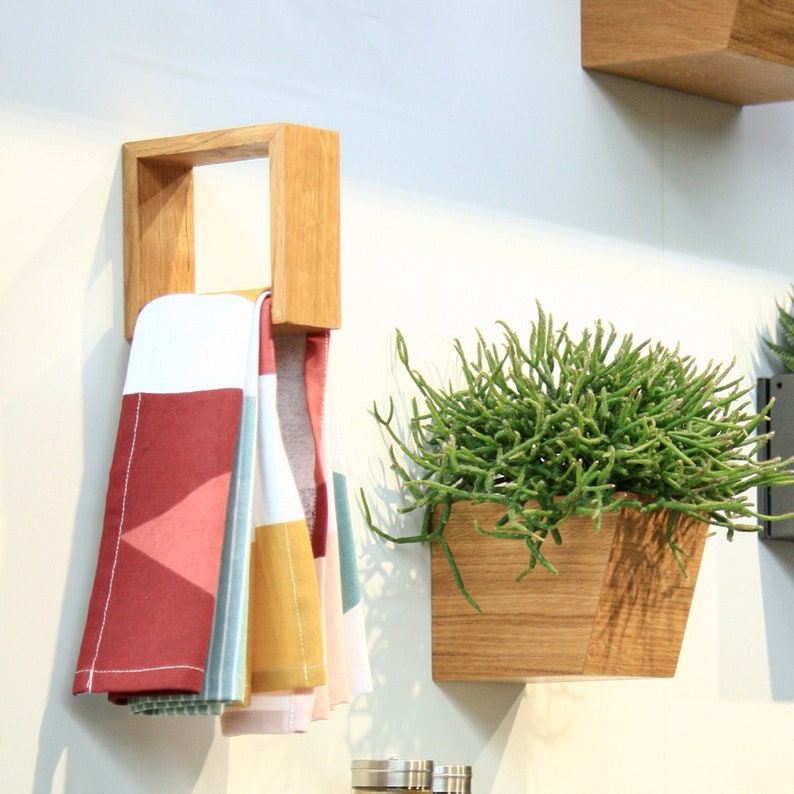 May include: A wooden wall-mounted shelf with a towel rack, holding three towels with geometric patterns in red, white, yellow, and blue. A wooden planter with a succulent plant is mounted on the wall below the shelf.