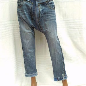 Puede incluir: Un par de pantalones vaqueros azules de mezclilla con un diseño único que presenta múltiples paneles de mezclilla cosidos juntos. Los pantalones tienen una cintura baja y un ajuste holgado.