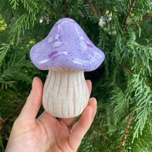 May include: A ceramic mushroom figurine with a purple and white speckled glaze. The mushroom has a white stem with a textured surface.