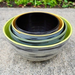 Może przedstawiać: Zestaw trzech gniazdujących misek w czarno-zielono-białe paski. Miski mają żółtą obwódkę.
