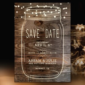 May include: Rustic wood background with a white outline of a mason jar with string lights. The text "THE SAVE DATE" is written in white with the date "SATURDAY APRIL 6TH 2019" and the names "ABRAM & JULIE ARE GETTING MARRIED BURNET, TX".