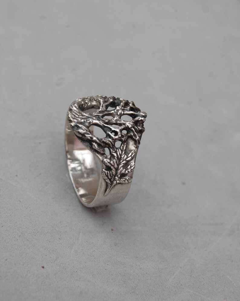 May include: A silver ring with a detailed tree design. The tree branches are intricate and delicate, creating a unique and eye-catching piece of jewelry.