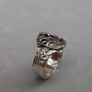 May include: A silver ring with a detailed design of a tree with leaves. The ring is made of metal and has a smooth finish.