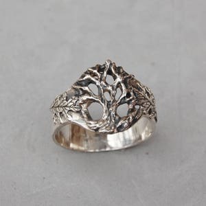 May include: A silver ring with a tree design. The tree is made of a delicate, openwork design and is surrounded by leaves.