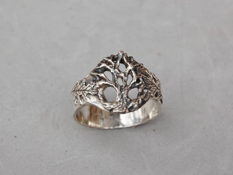 May include: A silver ring with a tree design. The tree is made of a delicate, openwork design and is surrounded by leaves.