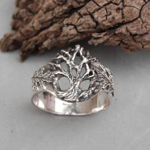 May include: A silver ring with a detailed tree design. The tree is made of intricate branches and leaves.
