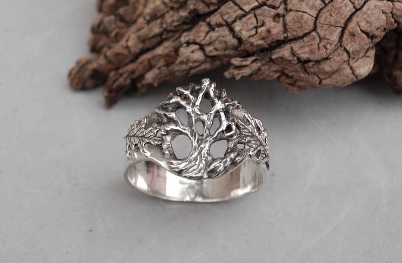 May include: A silver ring with a detailed tree design. The tree is made of intricate branches and leaves.