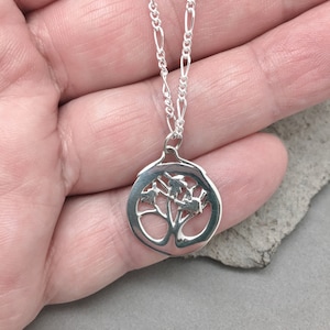 May include: A silver necklace with a tree of life pendant. The pendant is a circle with a tree design cut out of the center. The chain is a delicate silver chain.