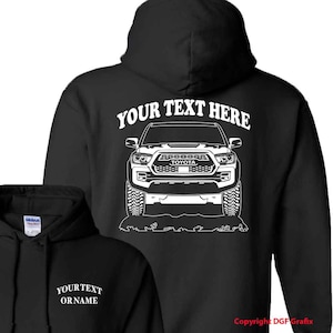 May include: Black hooded sweatshirt with a white outline of a Toyota Tacoma pickup truck on the back. The text "YOUR TEXT HERE" is above the truck. The text "YOUR TEXT OR NAME" is on the front of the sweatshirt.