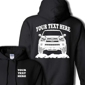 May include: Black hooded sweatshirt with a white outline of a Toyota Tacoma pickup truck on the back. The text "YOUR TEXT HERE" is above the truck. The front of the sweatshirt has the text "YOUR TEXT HERE" in white.
