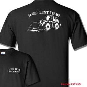 May include: Black t-shirt with a white outline of a front-end loader with the text "YOUR TEXT HERE" above it.