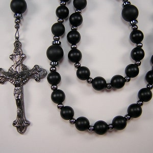 May include: A black onyx rosary with a silver crucifix featuring a depiction of Jesus Christ. The rosary beads are separated by silver spacers.