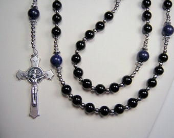 Può includere: Un rosario nero e argento con perline di pietre preziose blu. Il rosario presenta un crocifisso d'argento con una rappresentazione di Gesù Cristo.