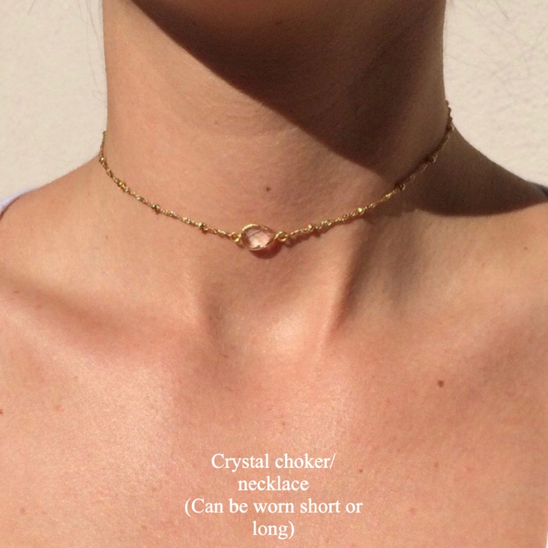 K&ouml;nnte beinhalten: Eine zarte goldene Ketten-Choker-Halskette mit einem einzelnen klaren Kristall-Anh&auml;nger. Die Halskette kann kurz oder lang getragen werden.