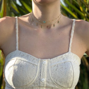 K&ouml;nnte beinhalten: Eine goldene mehrreihige Choker-Kette mit einem tropfenf&ouml;rmigen Anh&auml;nger aus gr&uuml;nem Stein und kleinen runden gr&uuml;nen Steinen, die an der Kette baumeln.