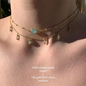 K&ouml;nnte beinhalten: Eine goldene Vermeil-Kristall-Choker-Kette mit einem tropfenf&ouml;rmigen Kristall-Anh&auml;nger und kleinen gr&uuml;nen Kristall-Anh&auml;ngern, die an der Kette h&auml;ngen.