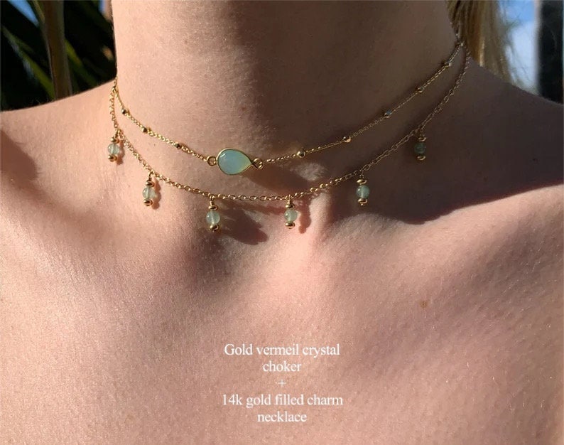 K&ouml;nnte beinhalten: Eine goldene Vermeil-Kristall-Choker-Kette mit einem tropfenf&ouml;rmigen Kristall-Anh&auml;nger und kleinen gr&uuml;nen Kristall-Anh&auml;ngern, die an der Kette h&auml;ngen.