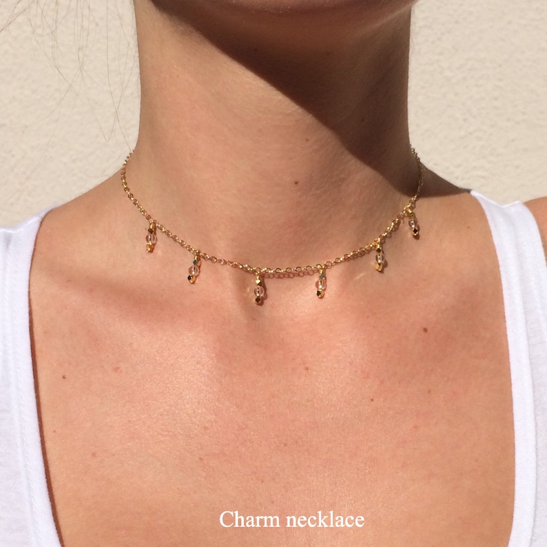 K&ouml;nnte beinhalten: Eine goldene Kettenkette mit kleinen, durchsichtigen Glasperlen, die daran h&auml;ngen. Die Kette befindet sich am Hals einer Person. Charm-Halskette.