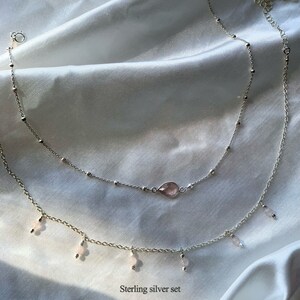 K&ouml;nnte beinhalten: Ein zartes Silber-Halsketten-Set mit einem rosa Edelstein-Anh&auml;nger und kleineren rosa Edelstein-Akzenten. Die Halskette ist mit einer k&uuml;rzeren Kette und einer l&auml;ngeren Kette mit baumelnden Anh&auml;ngern geschichtet. Sterling Silber Set.
