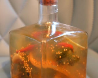 May include: A clear glass bottle with a cork stopper filled with a yellow liquid and various ingredients, including red peppers, green herbs, and small white seeds.