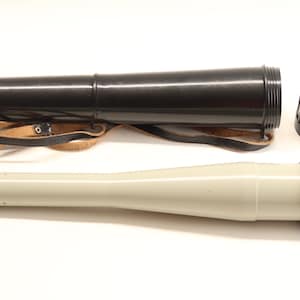 Può includere: Un telescopio nero con un cannone grigio e una custodia di trasporto nera. Il telescopio ha una cinghia in pelle e la custodia ha un tappo nero.