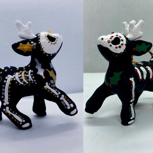 以下が含まれることがあります： 死者の日のテーマで描かれた、黒と白でペイントされた鹿のオーナメント2つ。1つの鹿は金色のアクセント、もう1つの鹿は緑と赤のアクセントが施されています。