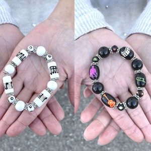May include: Two bracelets with black and white beads. One bracelet has musical notes and the other has musical instruments.