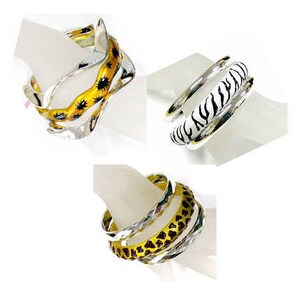 May include: Three silver bangles with different animal print designs. The bangles are stacked on top of each other. The designs include a zebra print, a leopard print, and a giraffe print.
