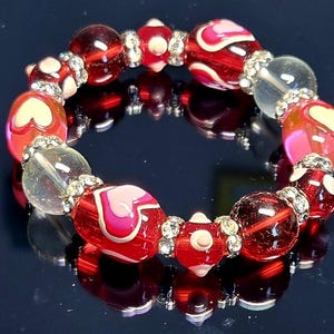 Puede incluir: Un brazalete de cuentas con cuentas rojas, transparentes y rosas. Algunas cuentas tienen dise&ntilde;os de coraz&oacute;n. El brazalete est&aacute; acentuado con espaciadores plateados. Las cuentas tienen aproximadamente 2 cm de di&aacute;metro.