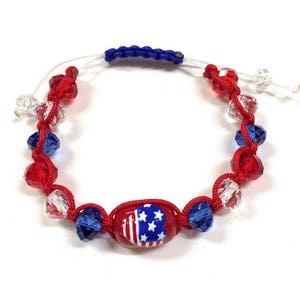 Puede incluir: Pulsera patriótica con cuentas rojas, blancas y azules. La pulsera tiene una cuenta ovalada central con un diseño de la bandera estadounidense. Las cuentas están ensartadas en un cordón rojo, con un cierre de cordón azul ajustable.