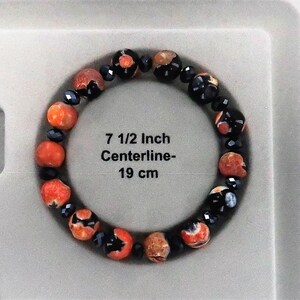 May include: A bracelet made of orange and black beads. The bracelet is 7 1/2 inches in circumference and has a centerline of 19 cm.